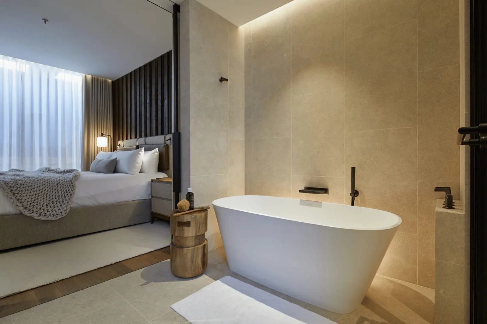 A 1 Hotel Mayfair freestanding white bath on stone tiles, open to the bedroom beside it