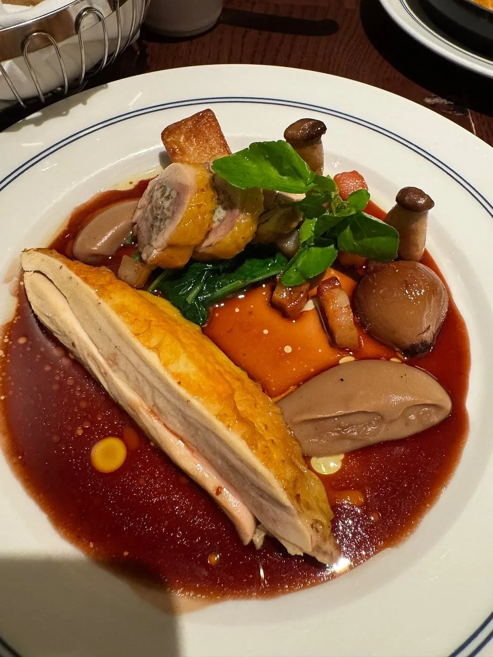 A chicken breast with crisp skin and a slice of stuffed ballotine in a glossy red wine sauce, with mushrooms, glazed shallots, watercress and a quenelle, on a blue-rimmed plate
