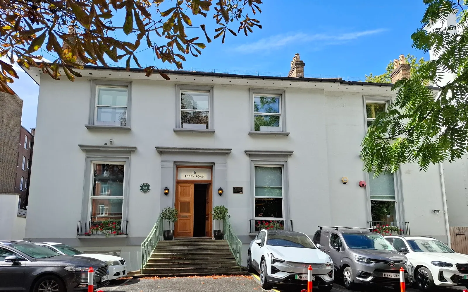 The white Georgian frontage of Abbey Road Studios, with 'Abbey Road' lettered above the wooden entrance door and cars parked outside