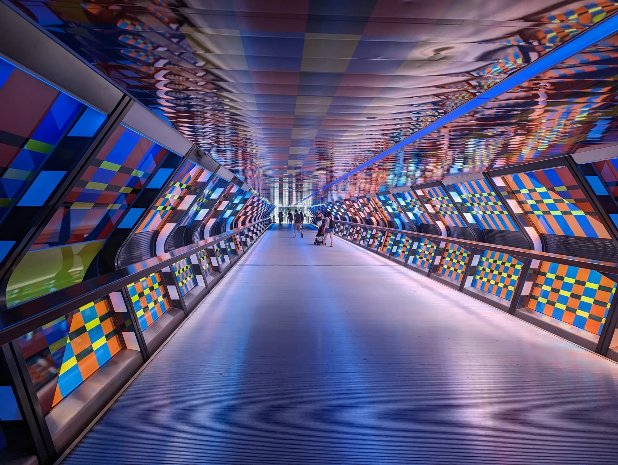 The interior of Adams Plaza Bridge at Canary Wharf, a mirrored tunnel lined with bands of coloured glass