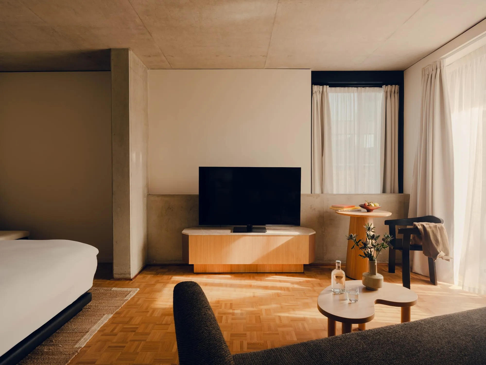 A room at Aethos London Shoreditch with a wood-fronted TV cabinet, a concrete accent wall and a floor-to-ceiling window