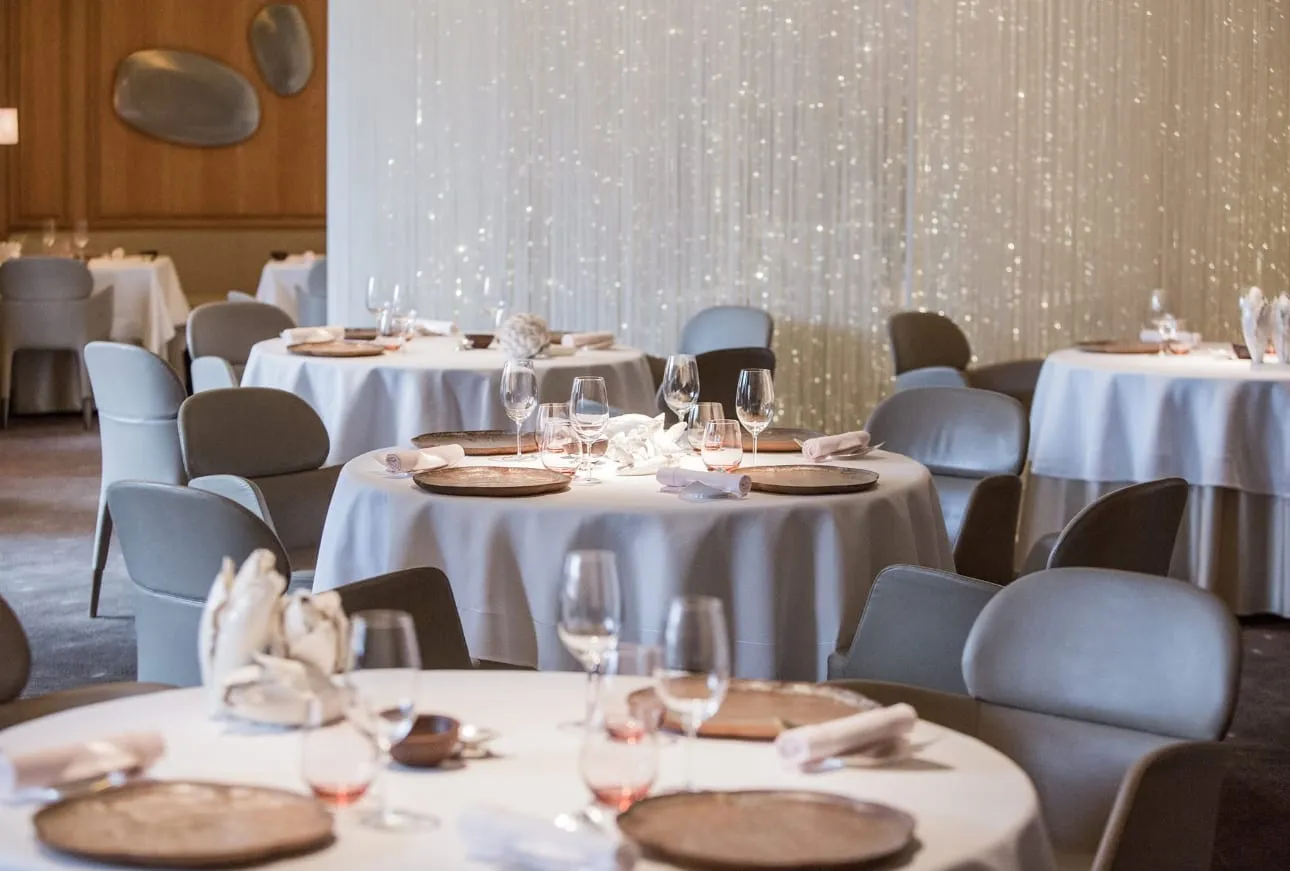 Round tables laid for dinner at Alain Ducasse at The Dorchester, with a curtain of fine lit strands behind them