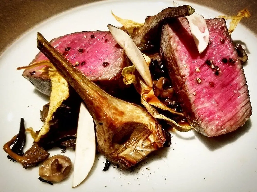 Two slices of rare-cooked beef with crisped artichoke, mushrooms and slivers of pear on a plain cream plate