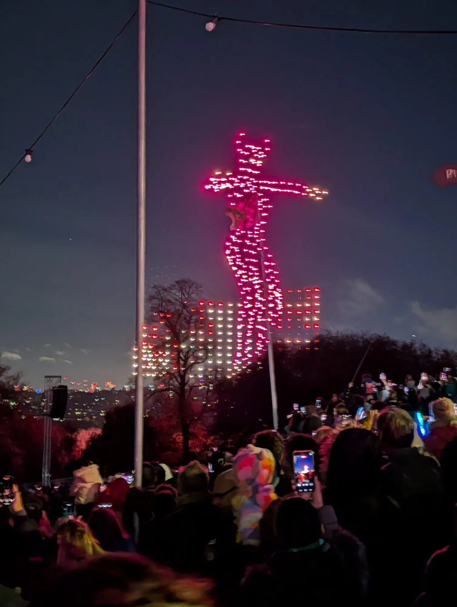 A drone display forming a lit figure in the night sky above Alexandra Park, watched by a crowd