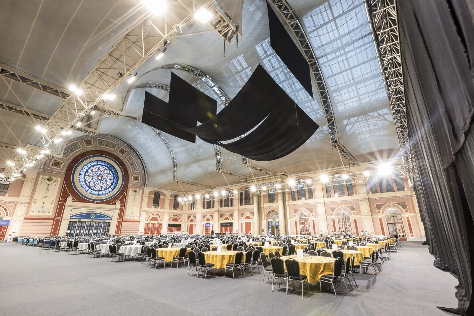 Alexandra Palace's Great Hall laid out for a banquet, round tables under its barrel-vaulted roof and stained-glass rose window