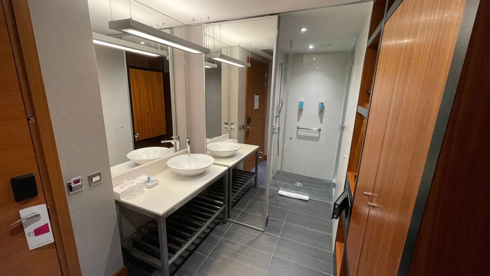 The bathroom at Aloft London ExCeL, with two basins on a shared counter and a glass-walled walk-in shower