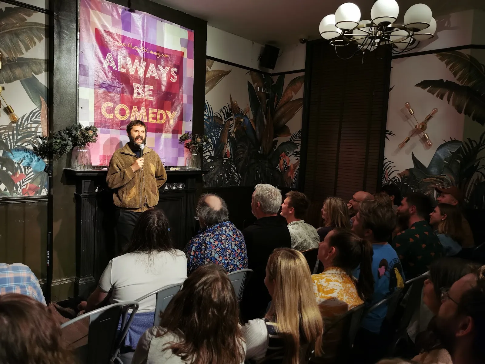 A comedian on the small stage at Always Be Comedy in Kennington, working a packed room from a few feet away