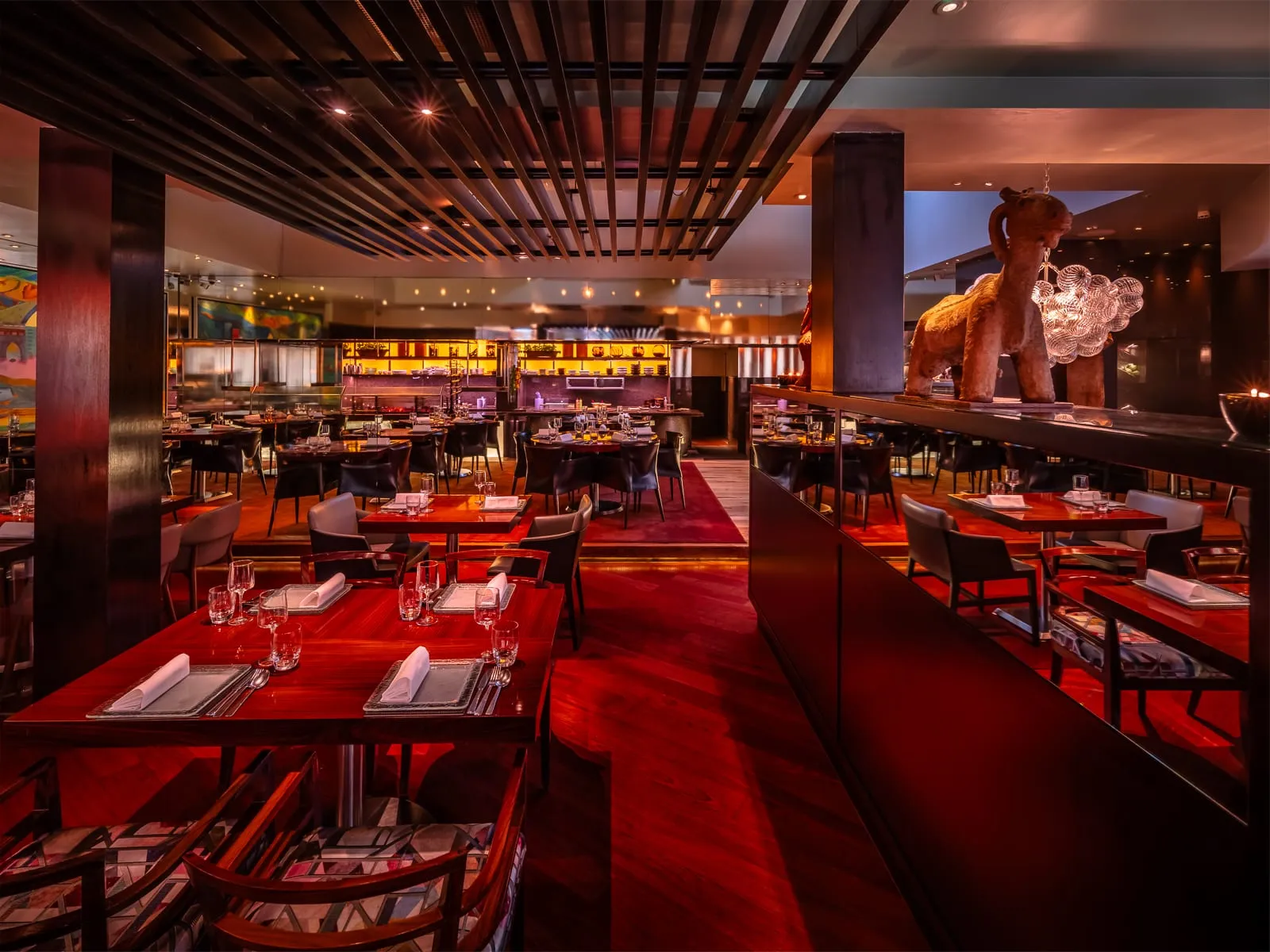 The dining room at Amaya in Belgravia with red polished tables and terracotta sculpture looking toward the open grill kitchen