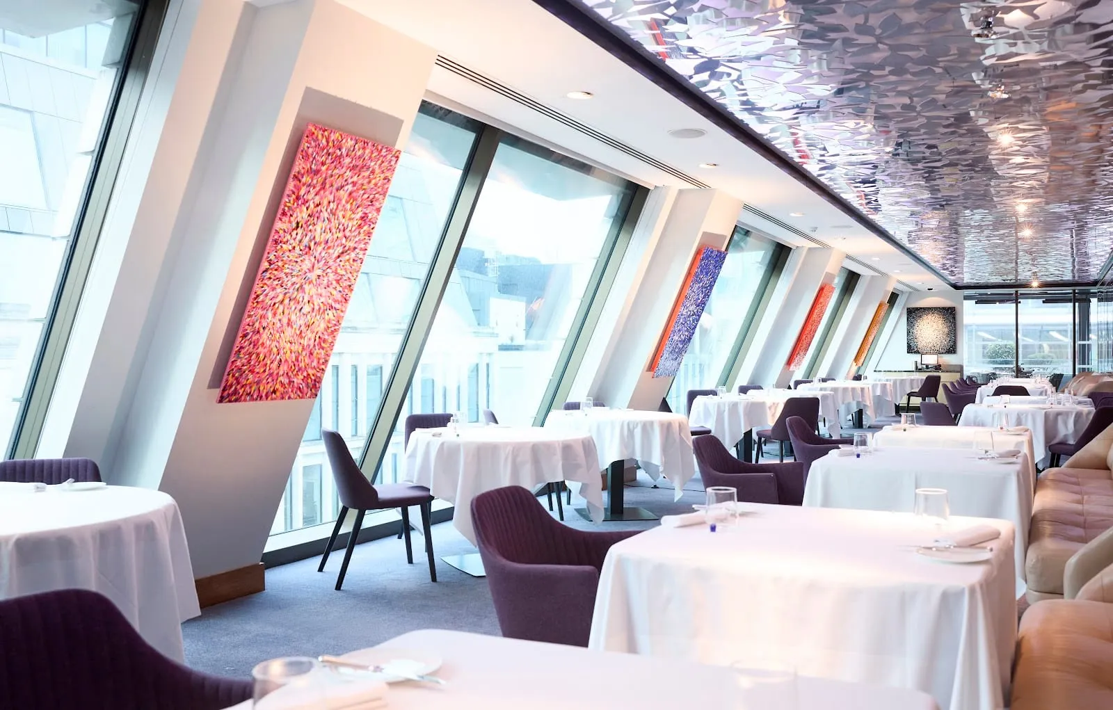 Angler's dining room: a row of outward-slanting windows down one side, white-clothed tables with purple armchairs, and a faceted mirrored ceiling running the length of the room