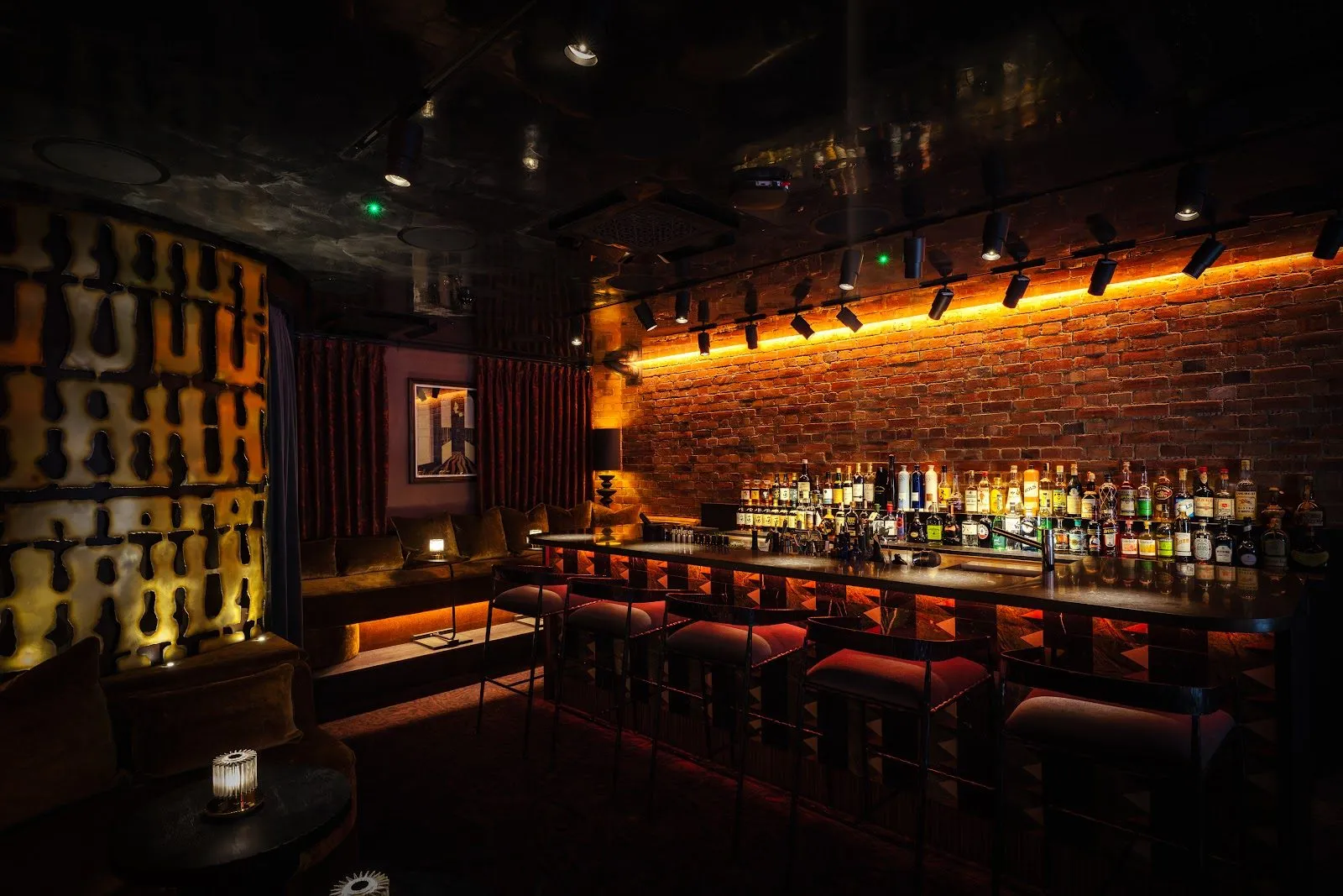 The bar at Archive & Myth, a long backlit counter with red-cushioned stools against a brick wall, under rows of spotlights
