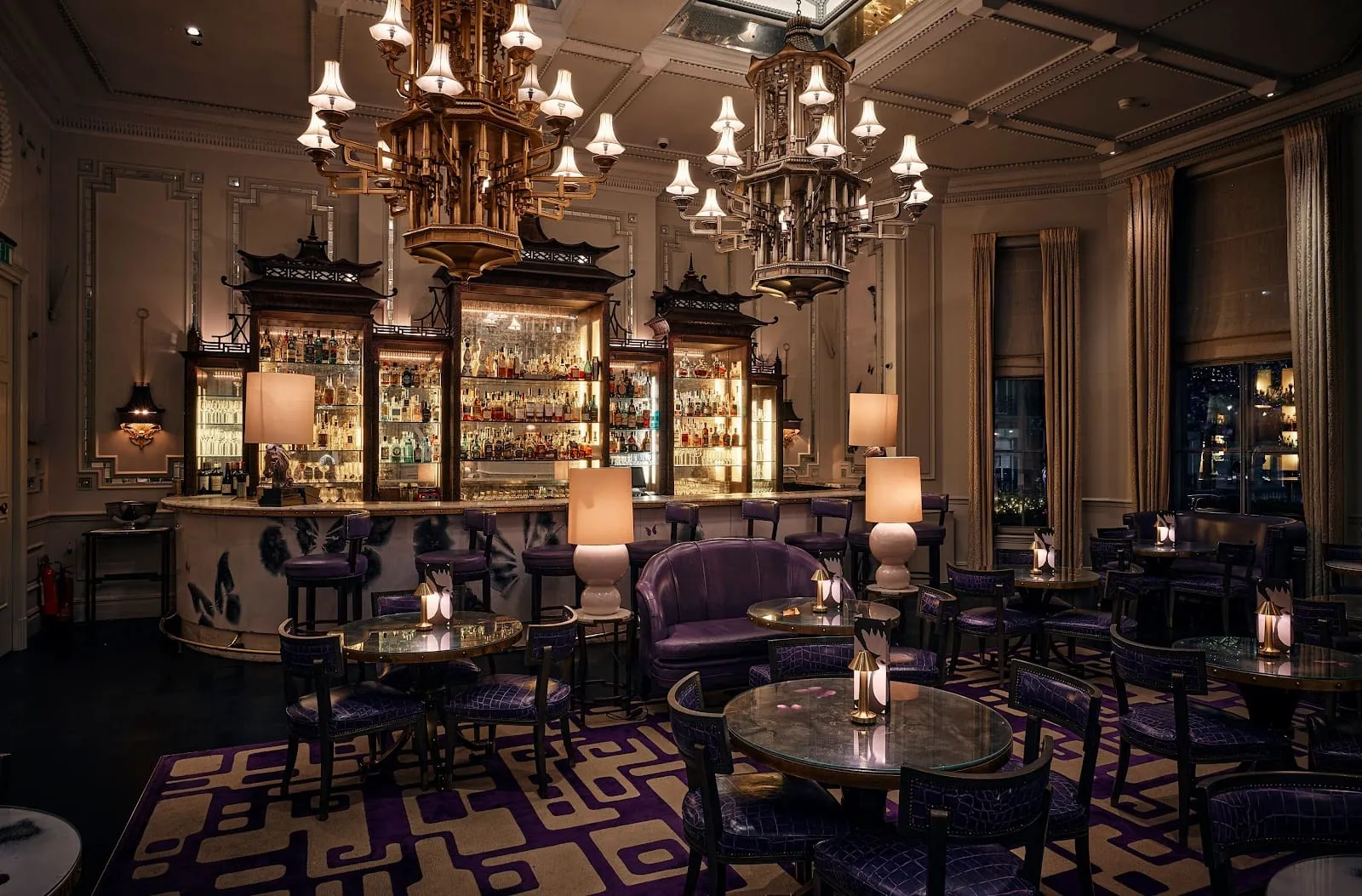 Artesian's back bar, a row of lit bottle cabinets topped with pagoda roofs, with two gold pagoda-shaped chandeliers above and purple leather chairs around small round tables