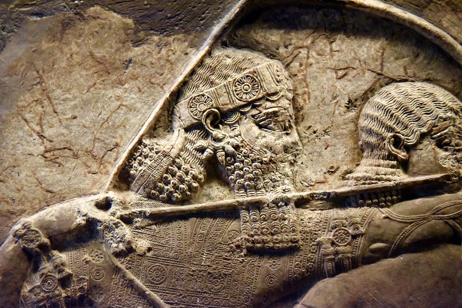 A close detail of an Assyrian relief showing King Ashurbanipal's bearded profile with a headband, drawing a bow