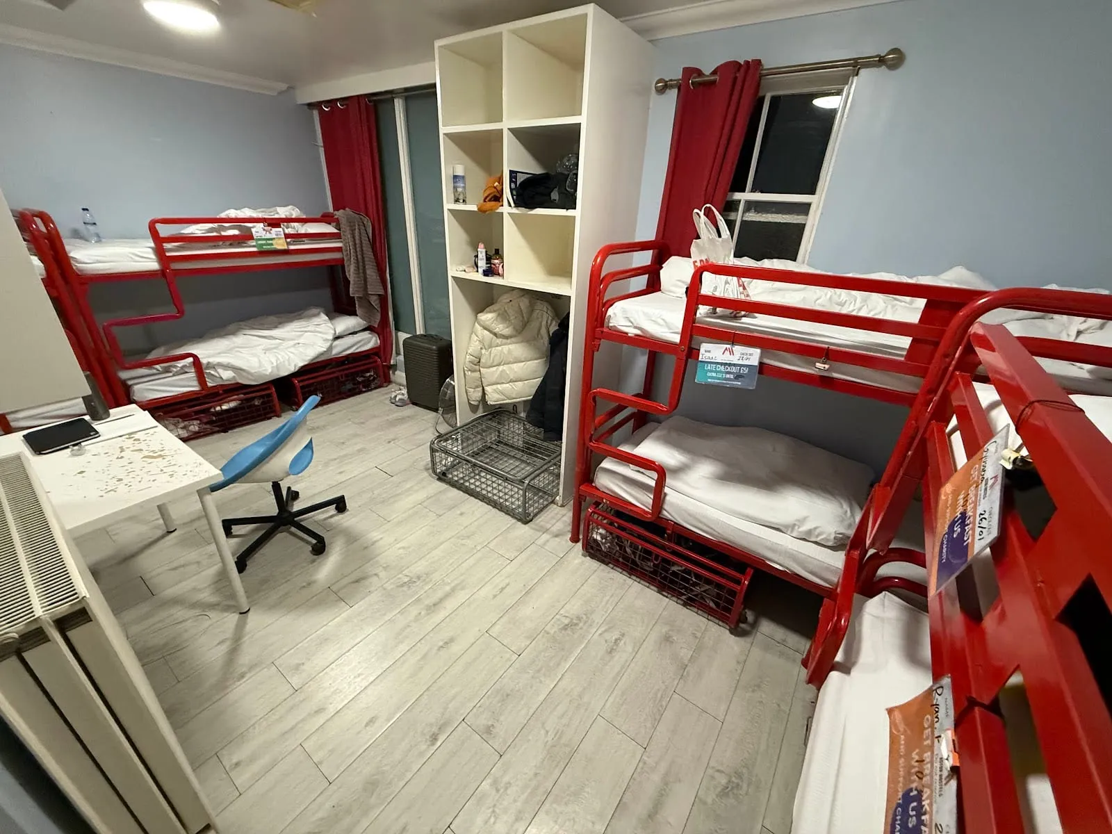 A shared dorm at Astor Victoria, with red-framed bunk beds either side of a communal storage unit