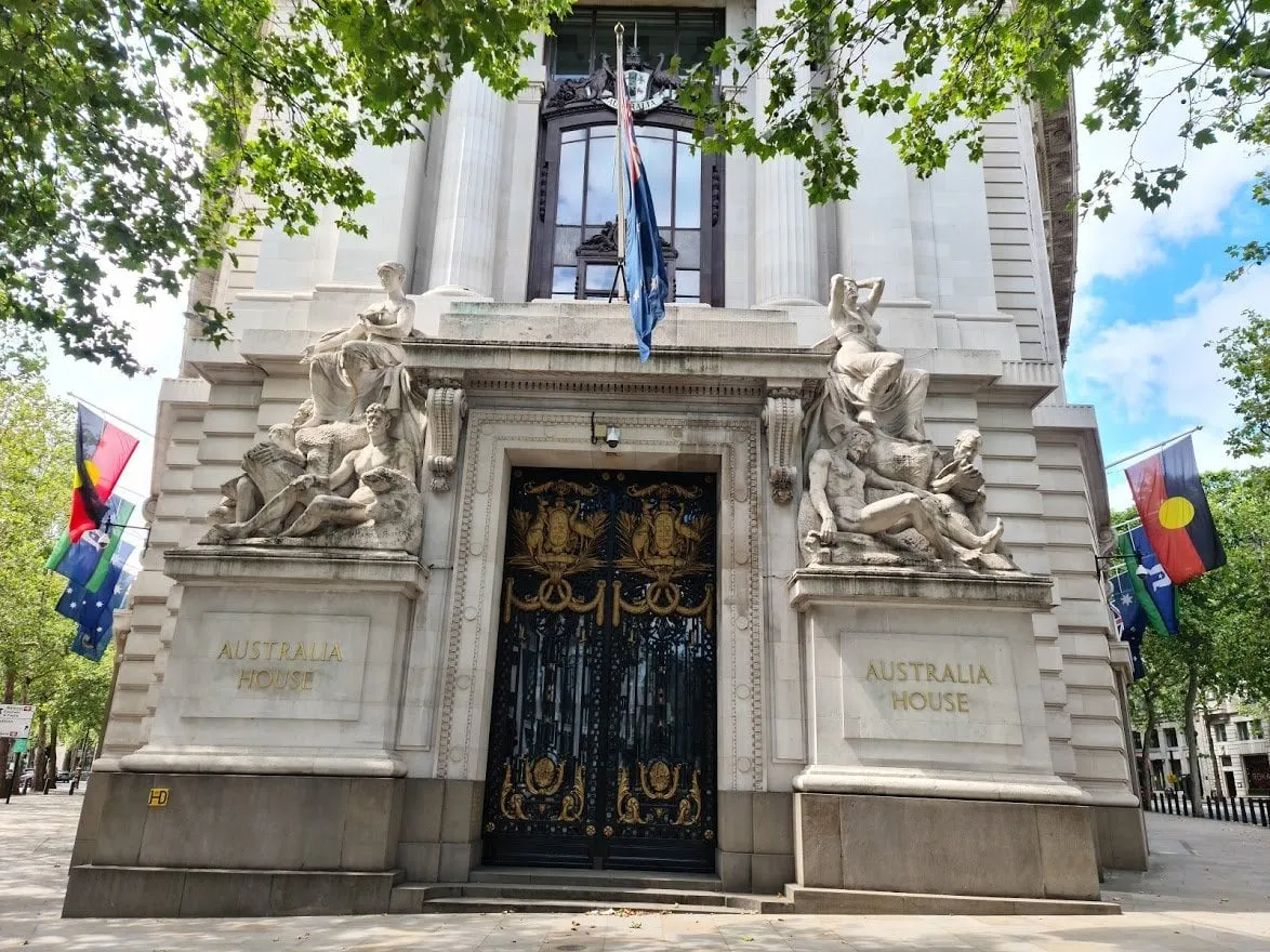 The stone entrance of Australia House, Australia House carved on the pedestals either side of black and gilt gates, sculpture groups above them and Australian, Aboriginal and Torres Strait Islander flags along the facade