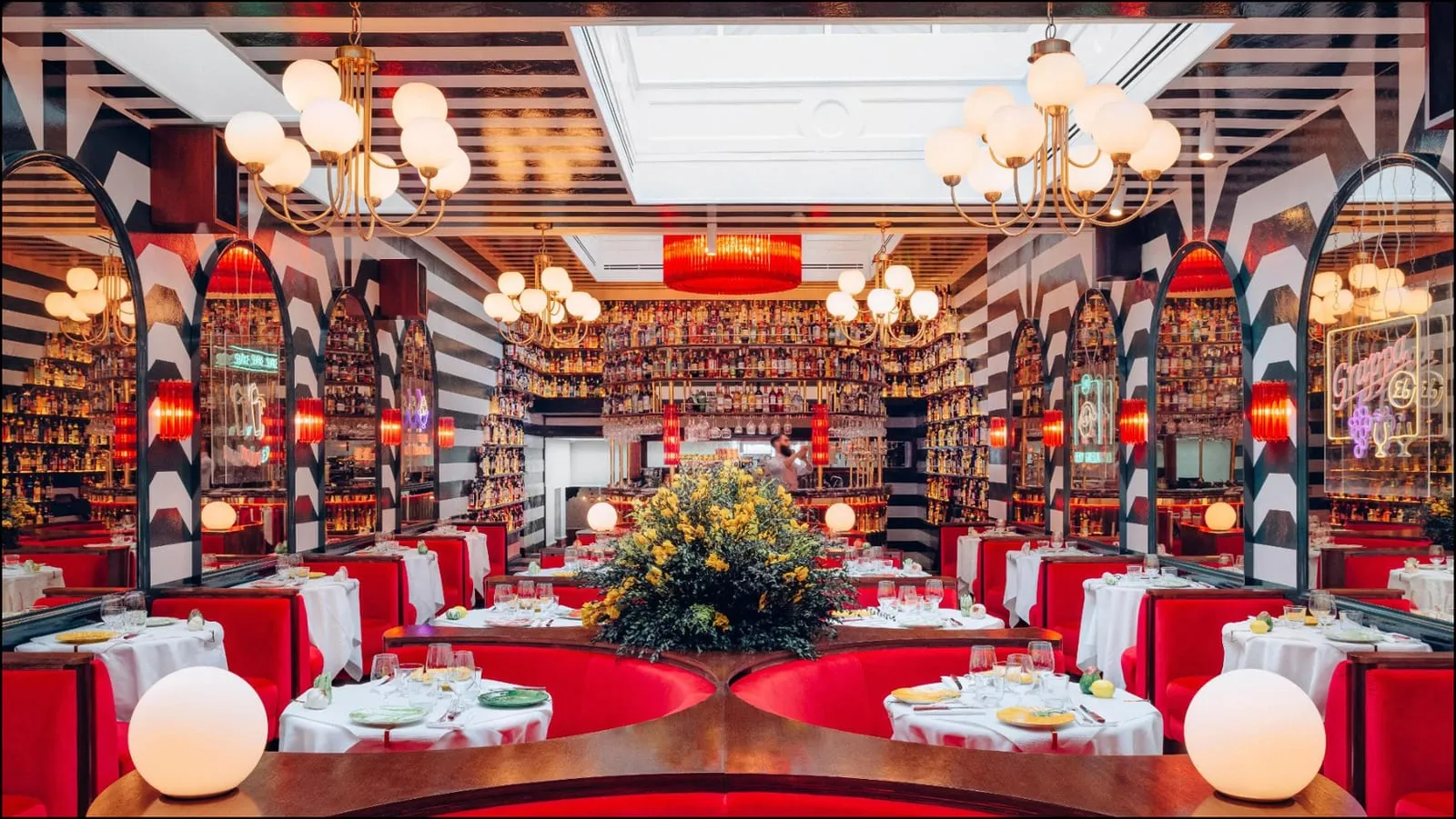 The main hall at Ave Mario, black-and-white striped walls and arches under globe chandeliers, with red velvet booths and walls of bottles behind