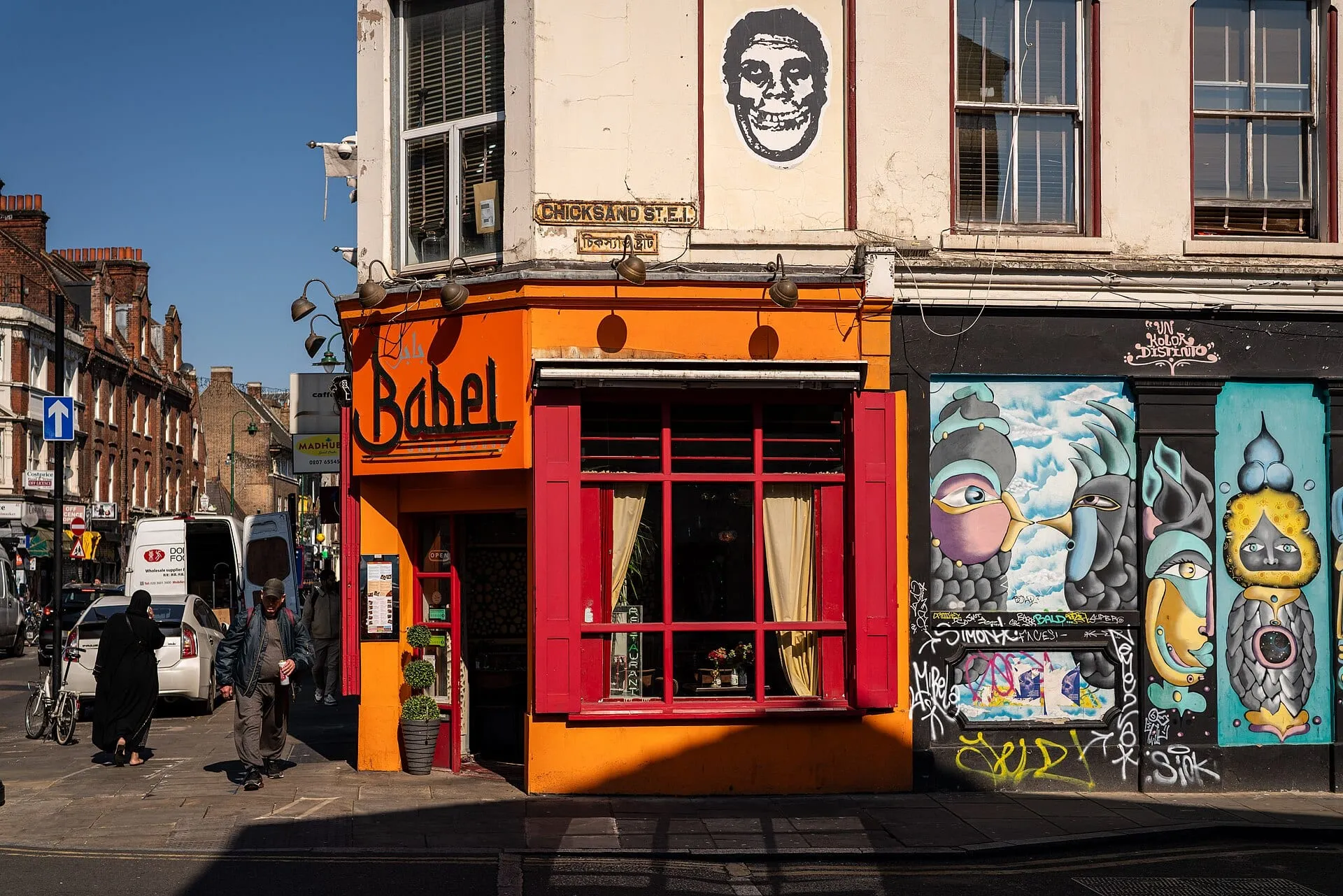 The orange and red corner frontage of Babel Grill House on Brick Lane, next to a street-art mural