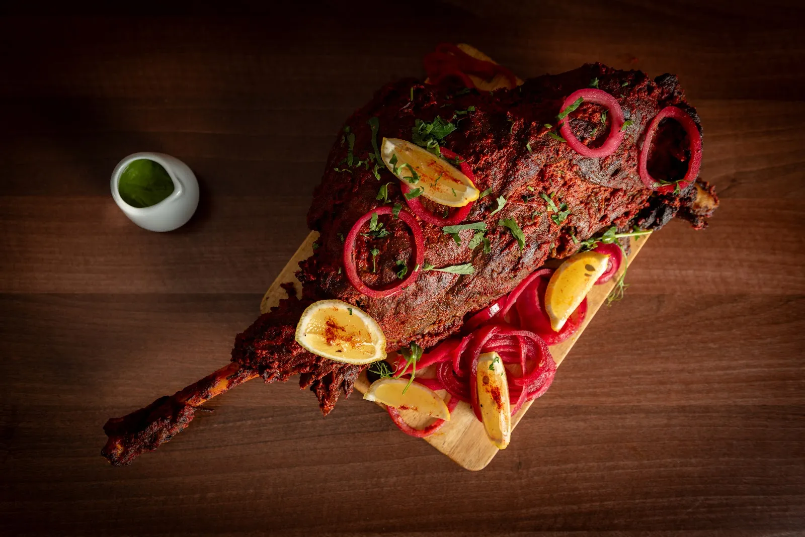 A slow-roasted whole leg of lamb raan with pickled red onions and mint sauce on a wooden board at Babur