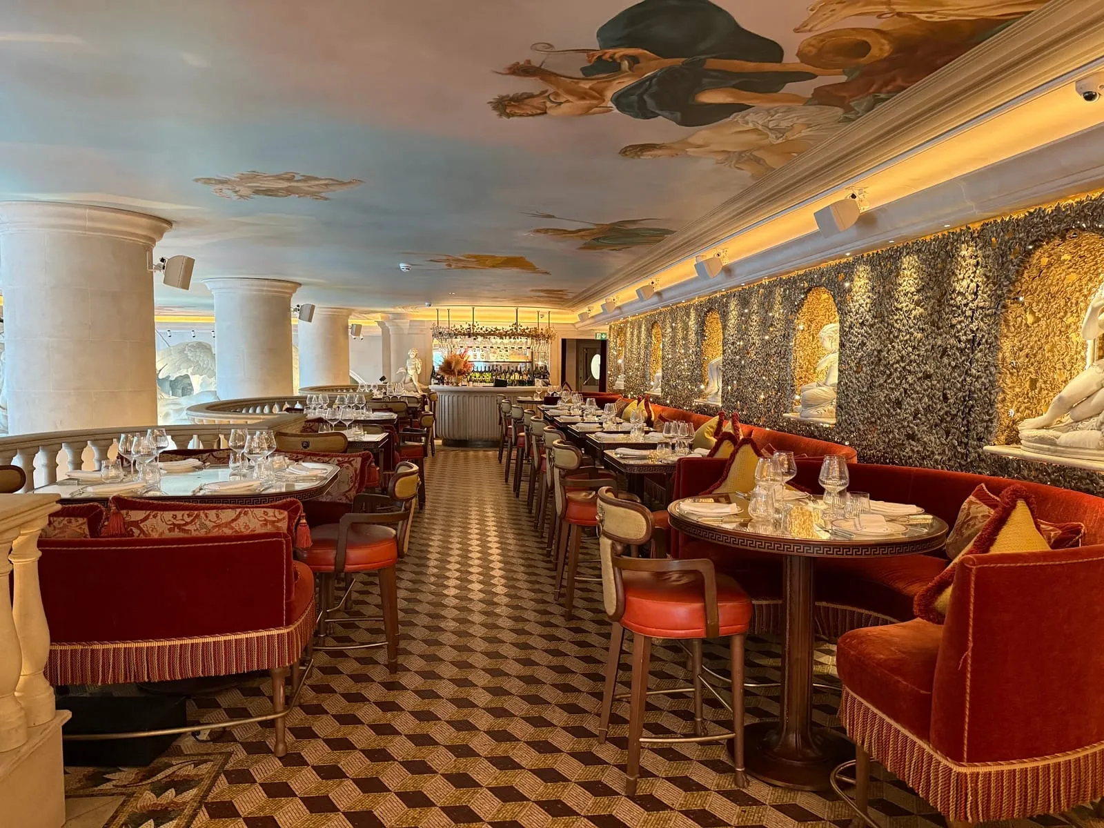 The long dining room at Bacchanalia, red velvet banquettes and tables beneath a hand-painted ceiling of classical figures, with white marble sculptures set into the grotto-style walls