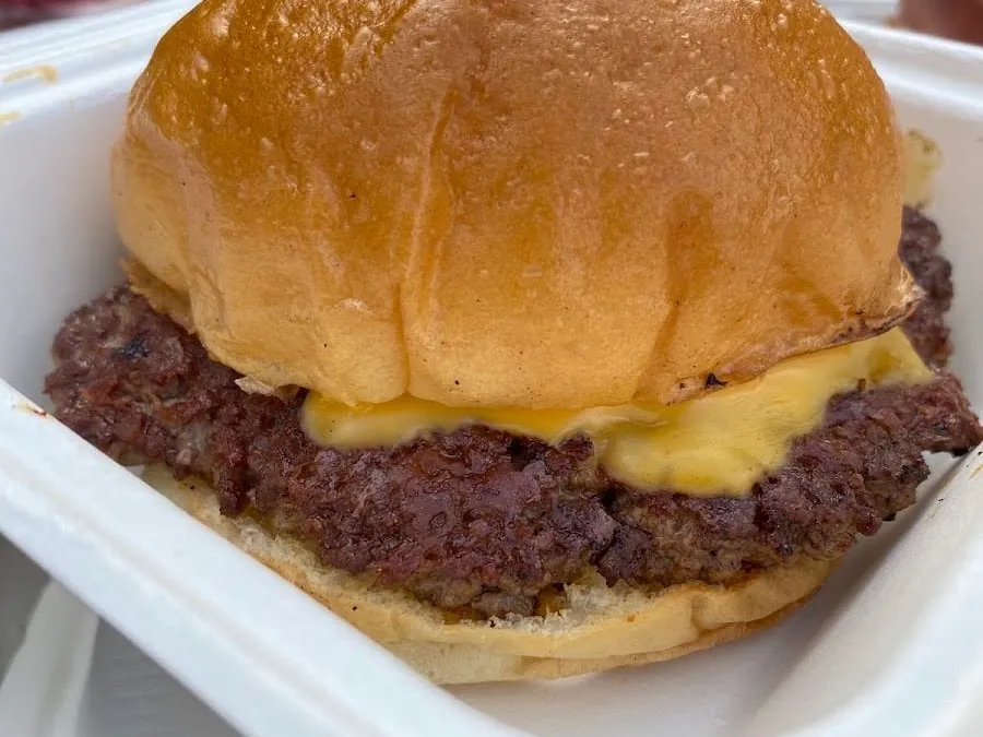 A close-up of Bake Street's smash burger in a white takeaway box: a wide, dark-crusted beef patty under a slice of melted American cheese in a glossy soft bun