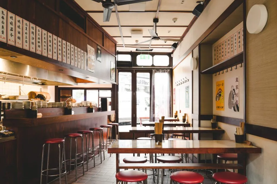 BAO Borough's narrow dining room, with red stools at a wooden counter, menu boards in Chinese characters along the walls and ceiling fans