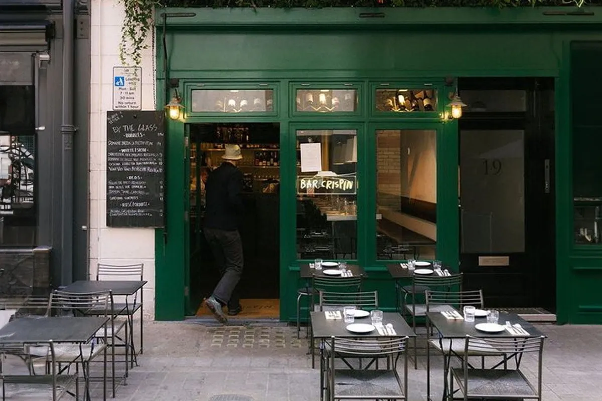 The green shopfront of Bar Crispin on Kingly Street, with a by-the-glass list chalked on a board outside and laid tables on the pavement