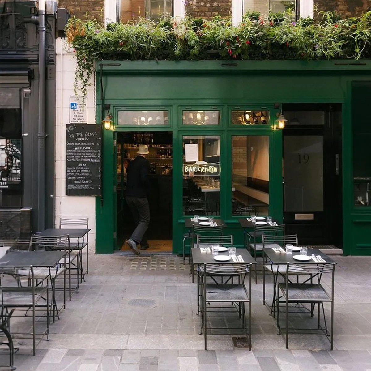 The green shopfront of Bar Crispin at 19 Kingly Street, with planted window boxes, a by-the-glass chalkboard and laid tables outside on the pavement