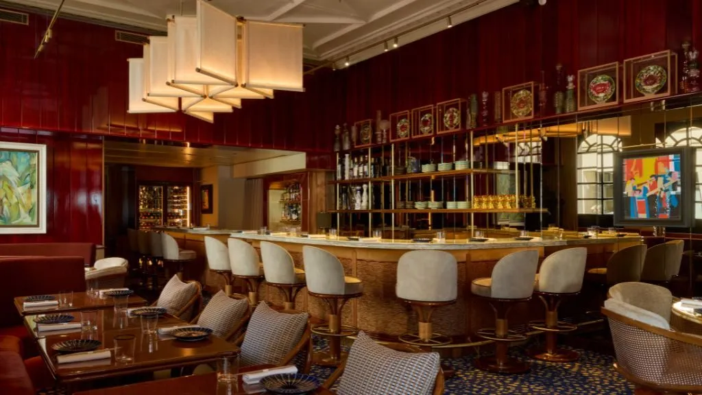 The dining room at Bar des Prés, with a long marble counter and cream bar stools, red lacquered walls, shelves of ceramics and paper lantern lights