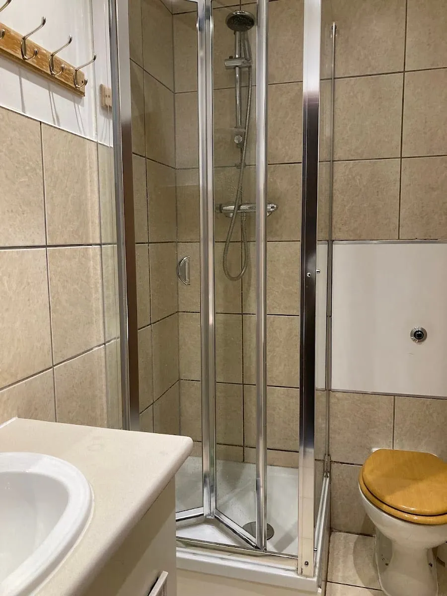 One of the bathrooms at Barmy Badger Backpackers, with a corner shower, beige tile and a wood-seat toilet