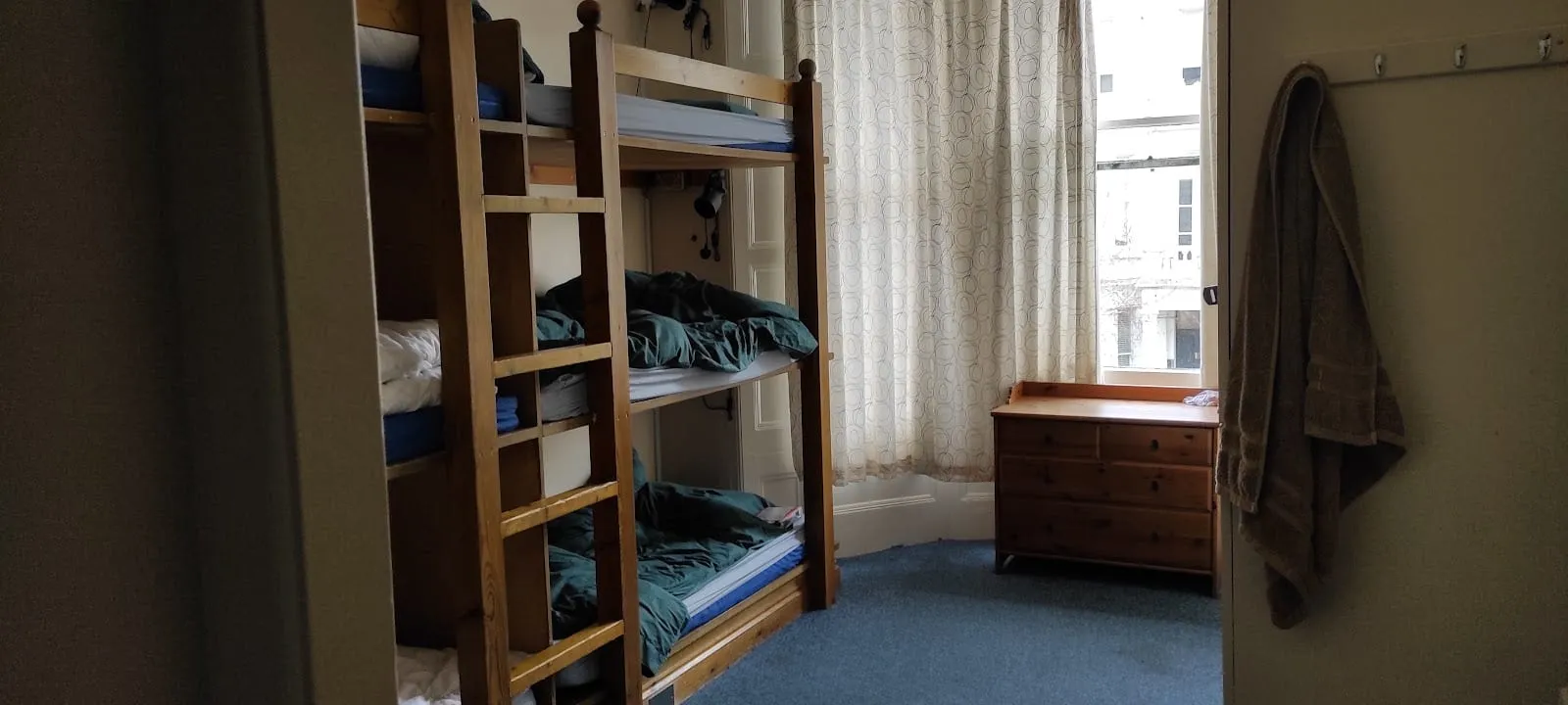 A bunk bed at Barmy Badger Backpackers, in wood with a ladder, beside a sash window and a chest of drawers
