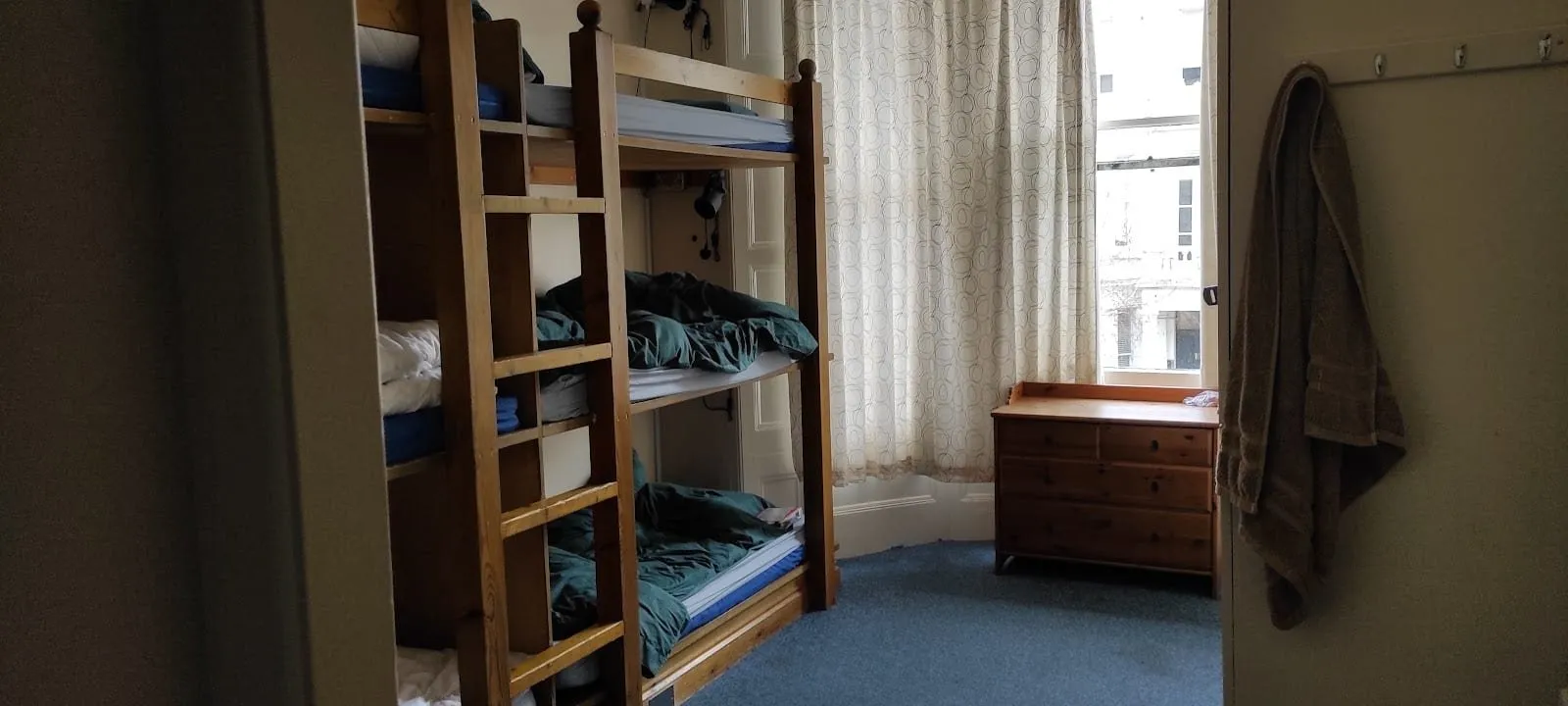 A Barmy Badger dorm with three-tier wooden bunks, green duvets, a pine chest of drawers in a bay window and a towel hanging on the door