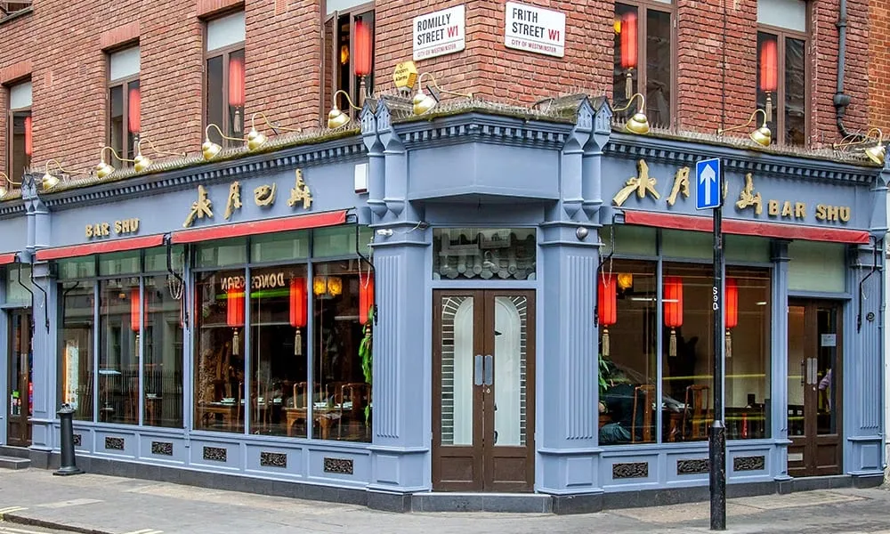 Bar Shu's blue-grey corner shopfront with red lanterns strung along the front and street signs for Frith Street and Romilly Street above
