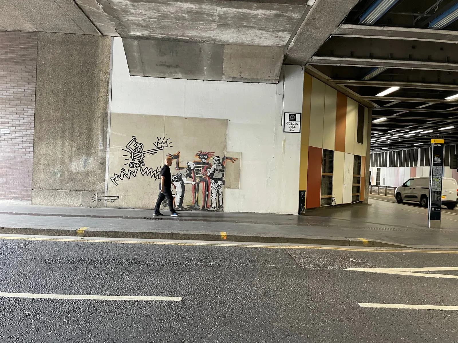 Banksy's second Basquiat mural on the wall of the Beech Street tunnel, police officers searching a Basquiat-style figure, with a Golden Lane sign on the pillar beside it