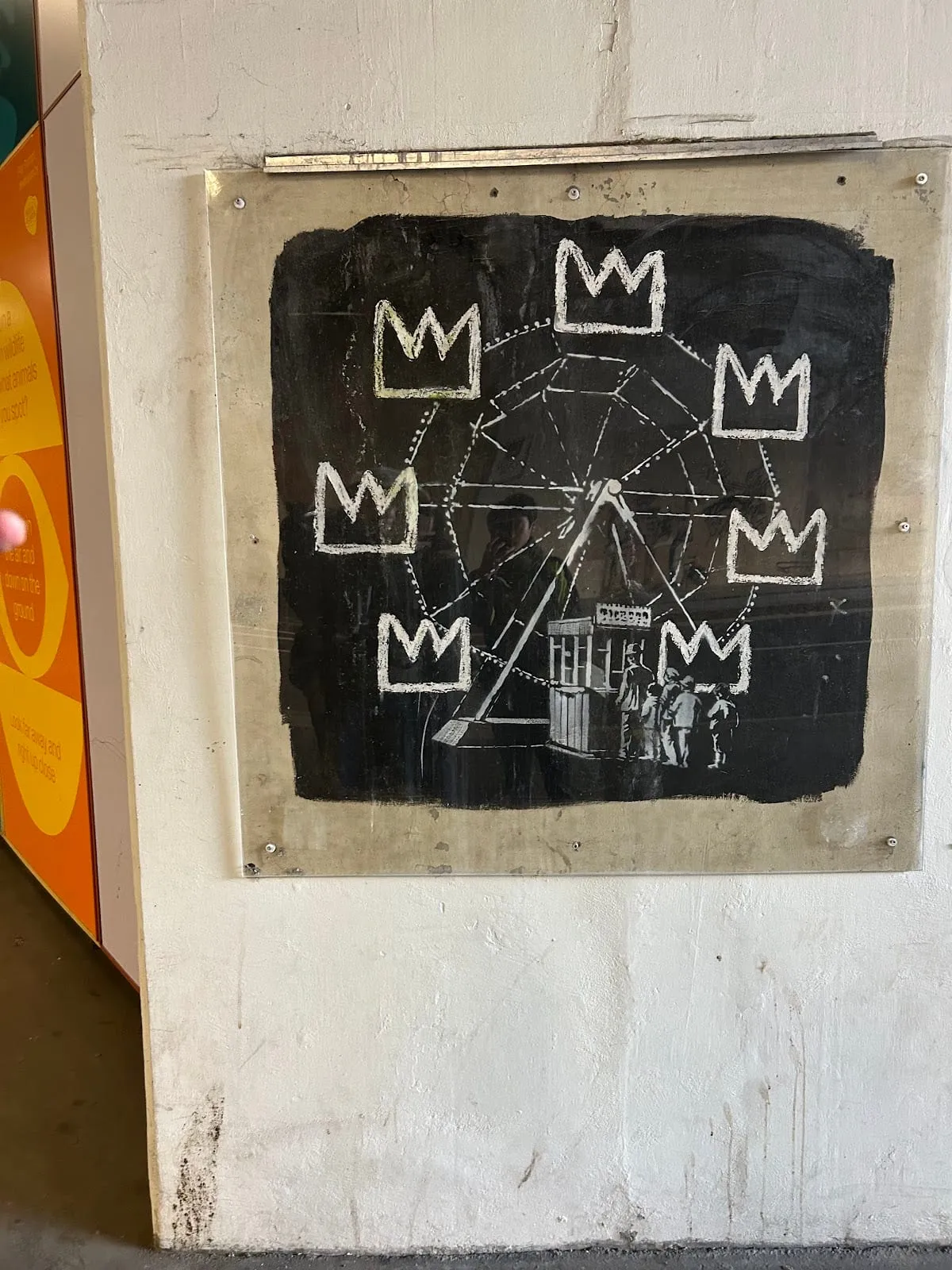 Banksy's Basquiat-style ferris wheel of white crowns on a black panel, fixed behind a clear screen on a white wall
