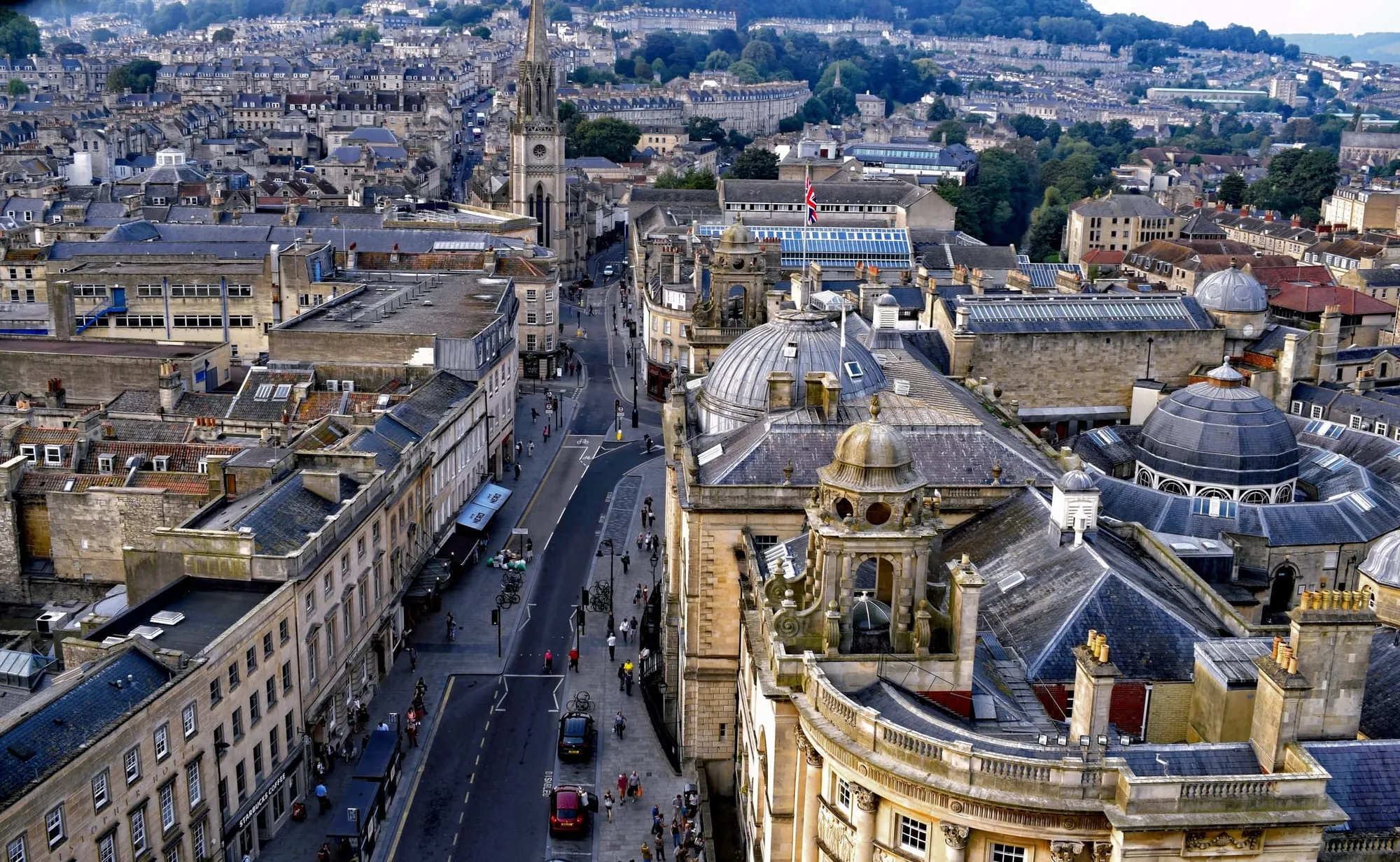 Bath from above: rooftops, the abbey tower and the main street running through the middle of the city, hills behind