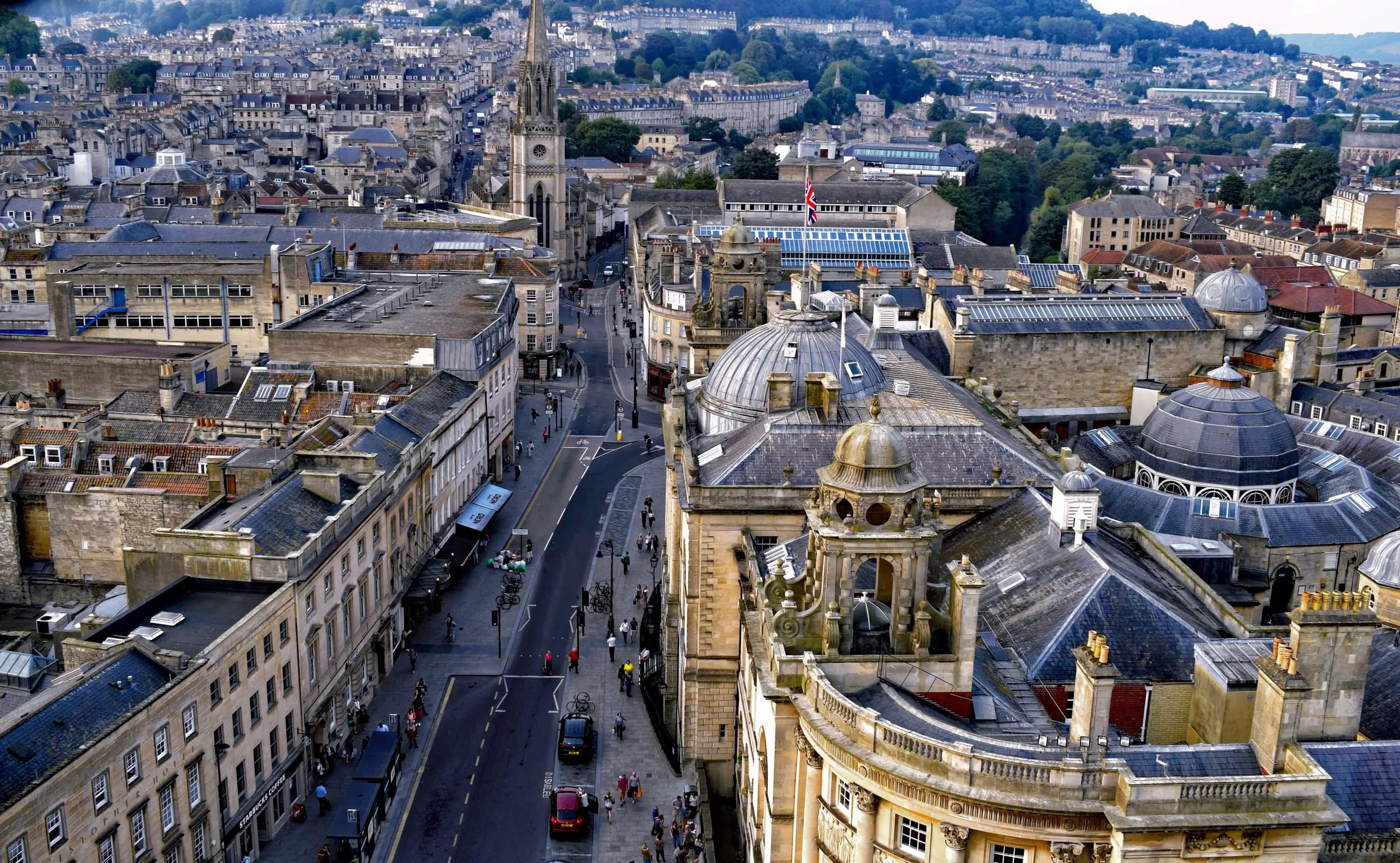 Bath from above: rooftops, the abbey tower and the main street running through the middle of the city, hills behind