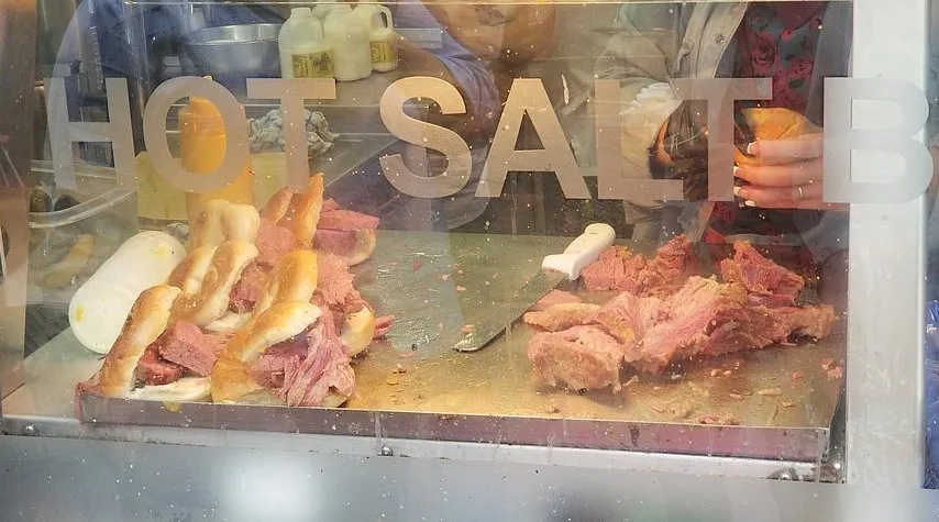 Salt beef being carved behind a hot salt beef window, with beigels filled and waiting