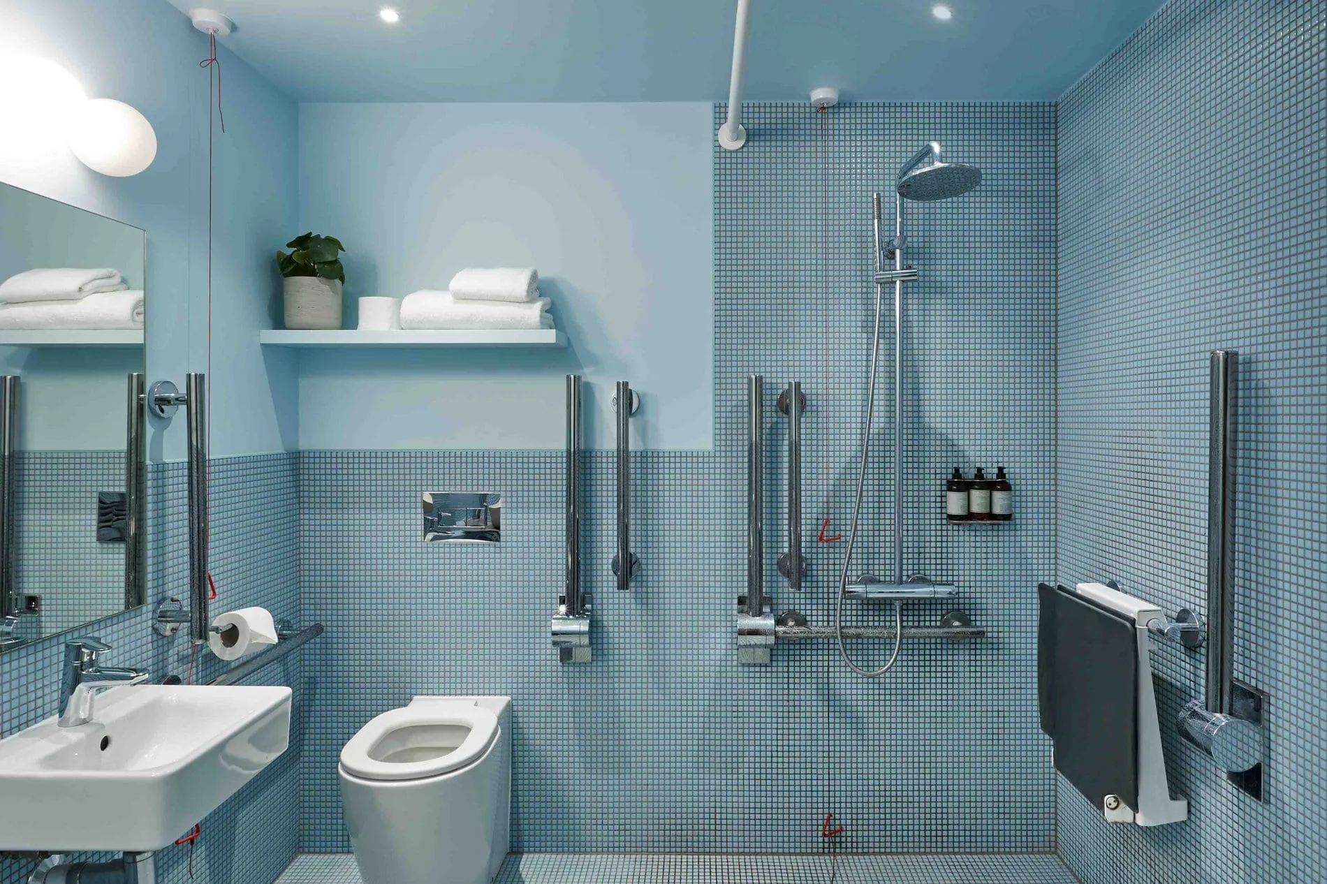 The bathroom at Bermonds Locke, with blue mosaic tile, a curbless shower and grab rails