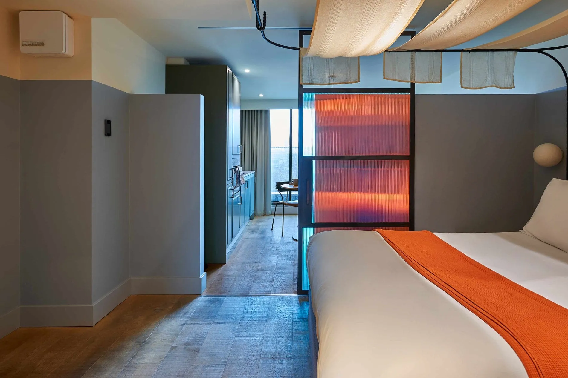 A room at Bermonds Locke, with a backlit glass panel dividing the bed area from the kitchenette beyond