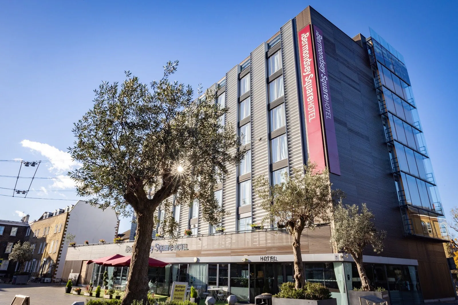 Bermondsey Square Hotel's angular grey and red facade above the antiques market square, with olive trees out front