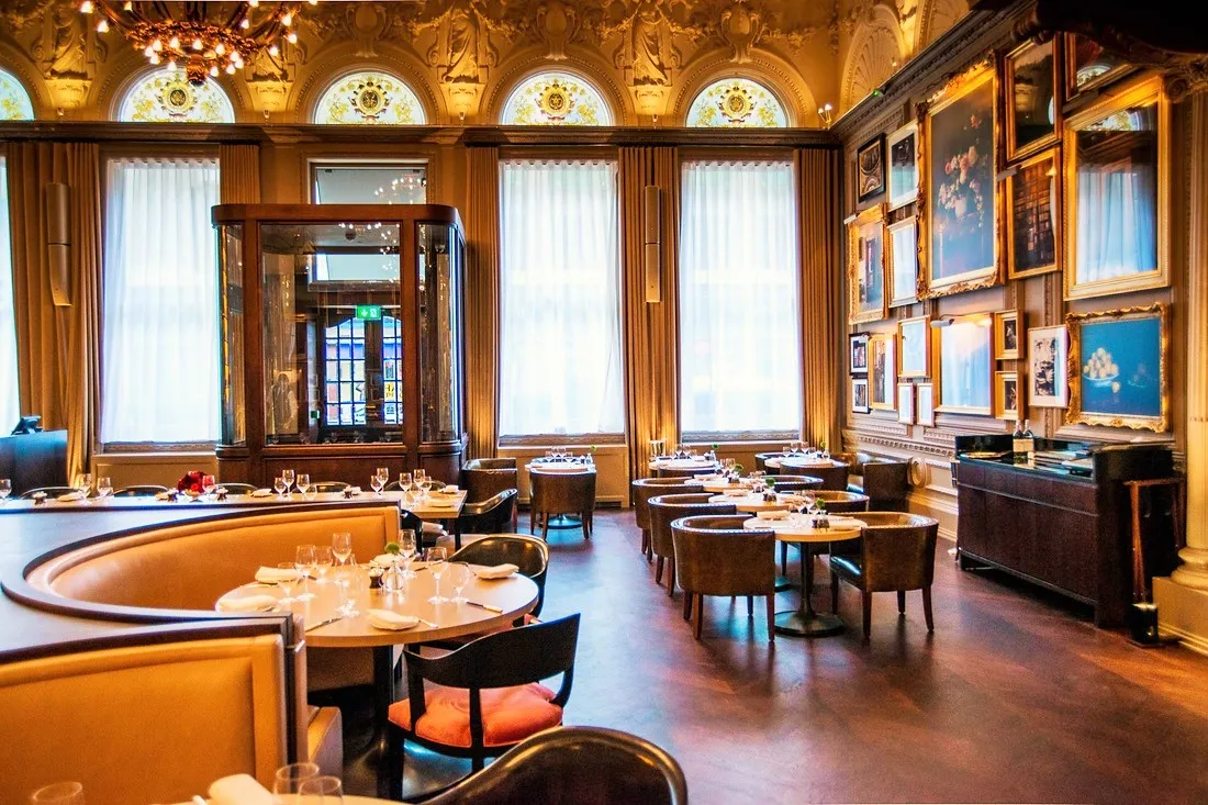 The empty dining room at Berners Tavern in daylight, tables laid beneath the gallery of framed pictures and ornate ceiling