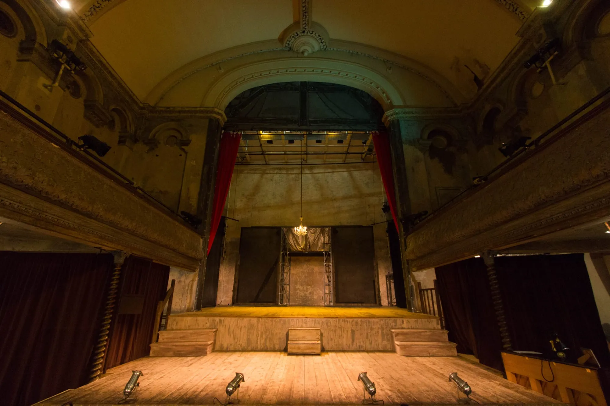 The bare stage and faded gilt balconies of Wilton's Music Hall, the oldest surviving grand music hall in the world, lit by a row of footlights