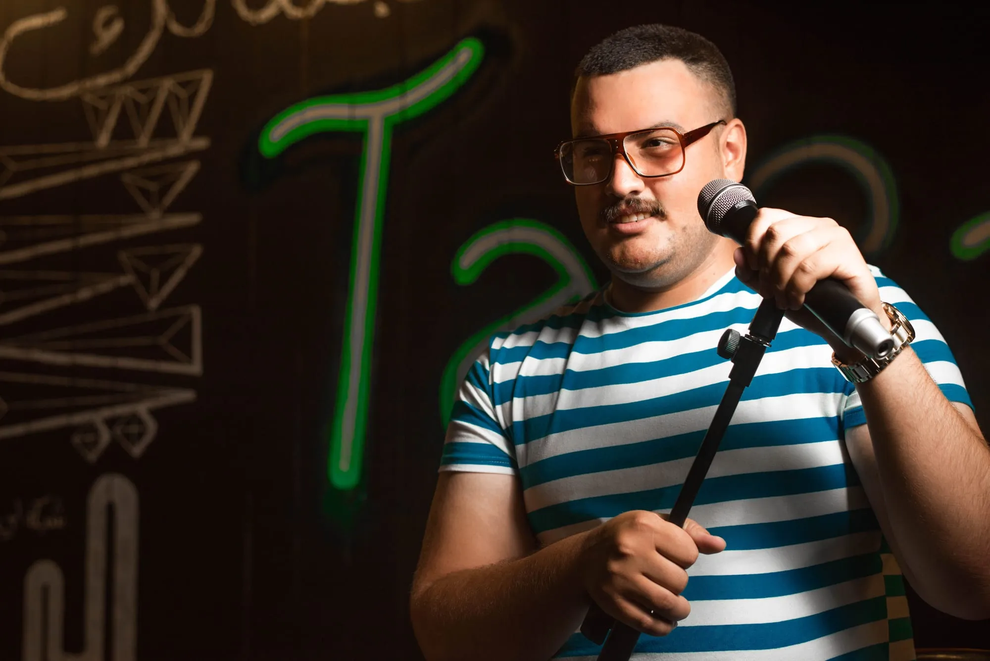 A stand-up comedian holding a microphone in front of a neon-lit wall