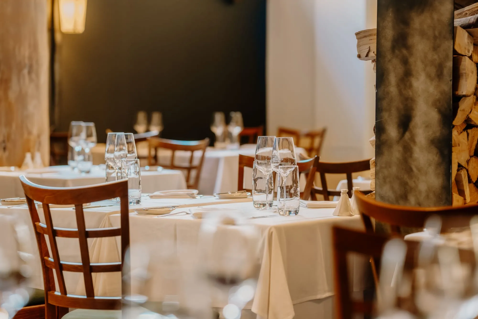 A bistro dining room laid with white tablecloths, wine glasses and wooden chairs