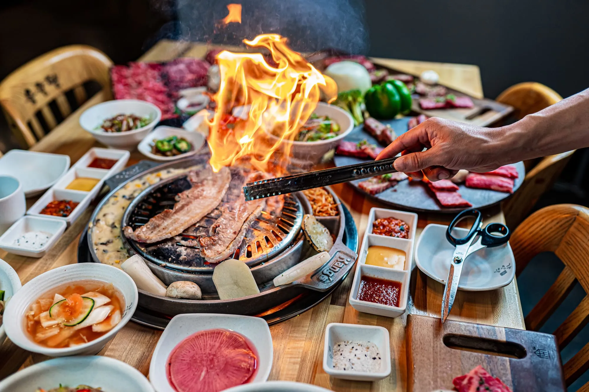 Meat flaming on a Korean barbecue grill surrounded by dishes of banchan