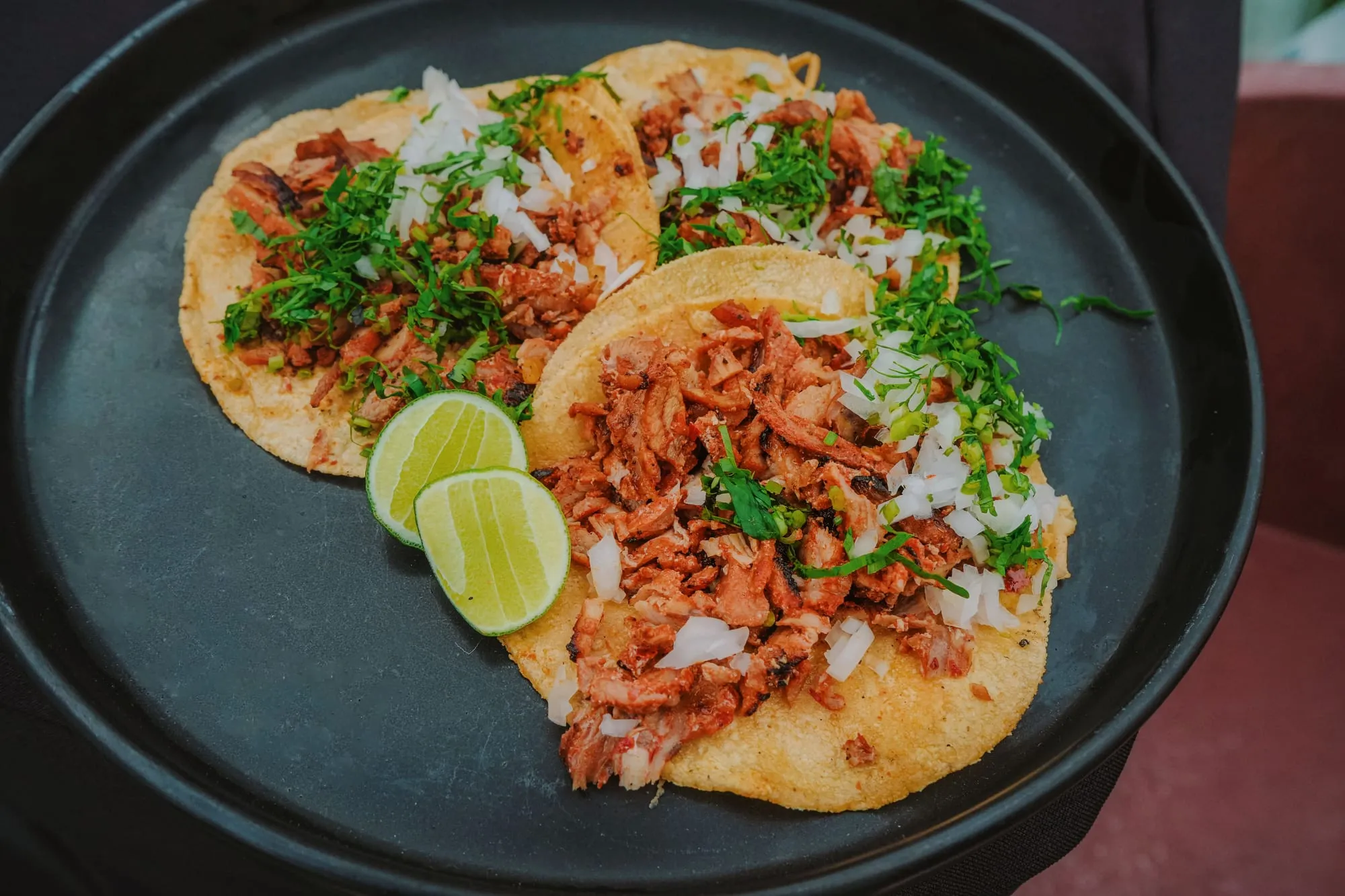 Tacos al pastor topped with onion and coriander, with lime wedges alongside