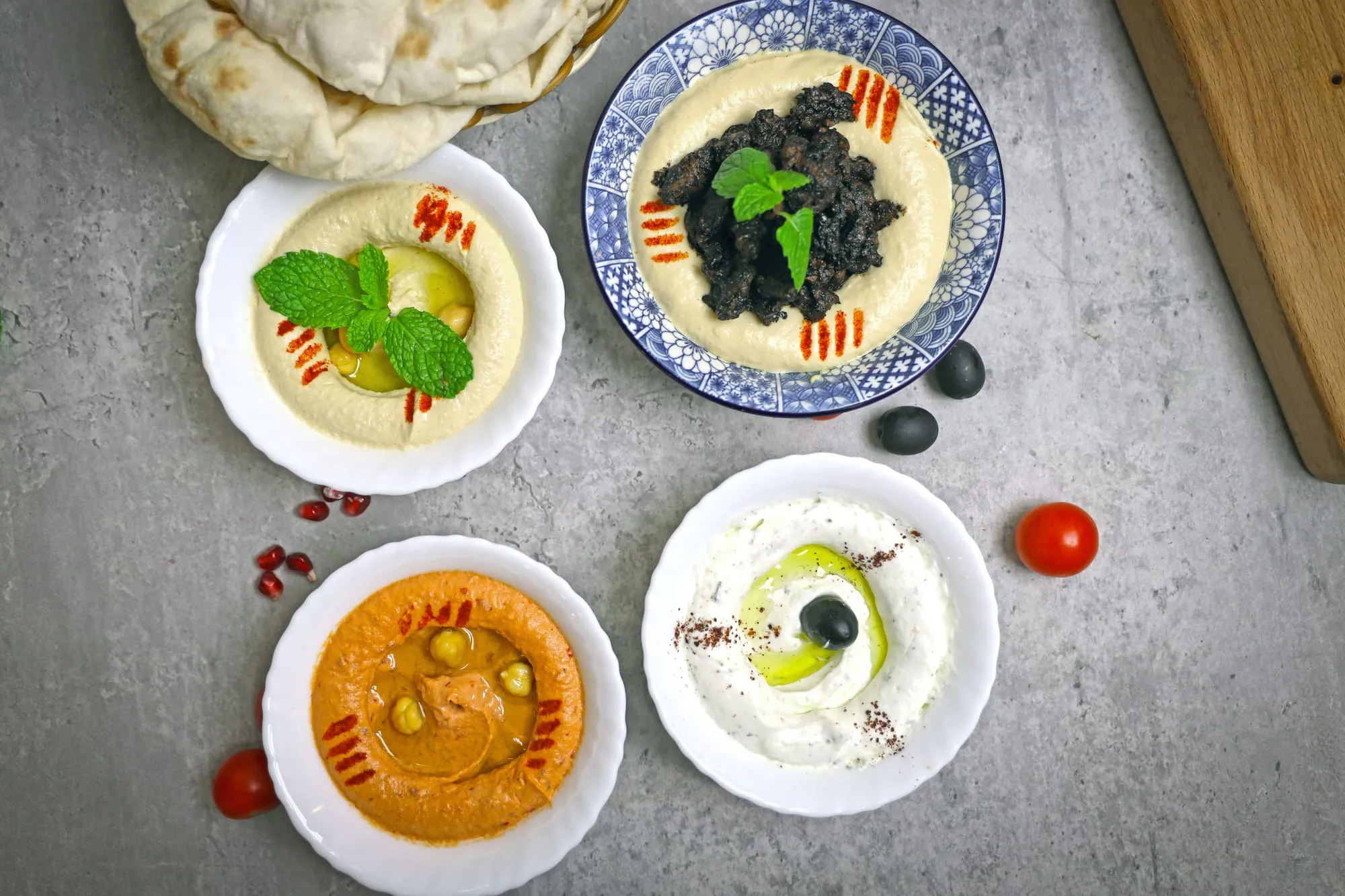 Bowls of hummus, muhammara and labneh with flatbread on a stone table