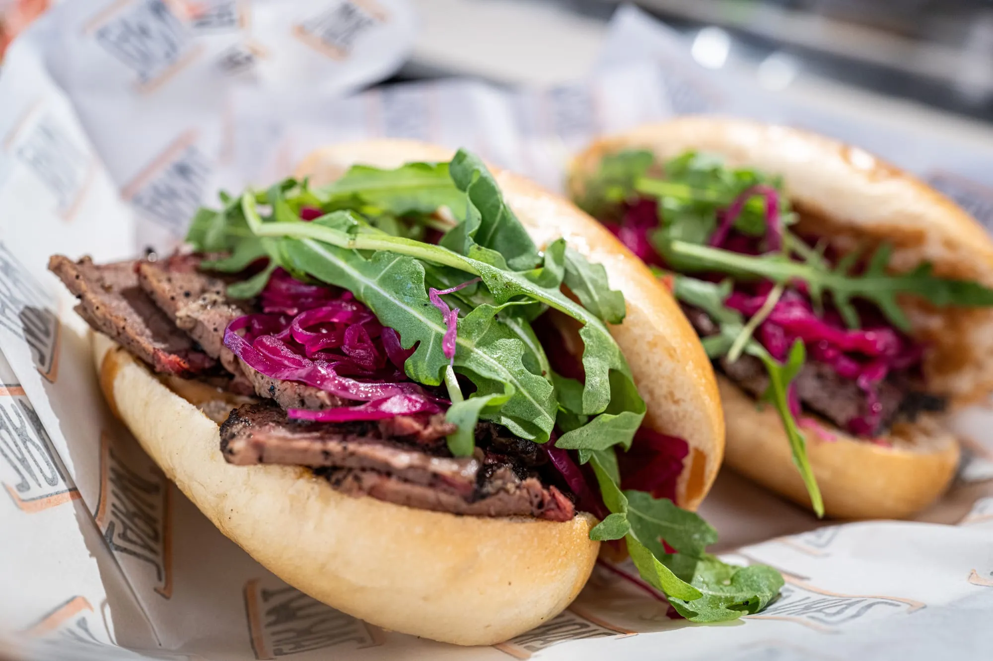 A pastrami sandwich with pickles and salad in a soft bun, cut in half