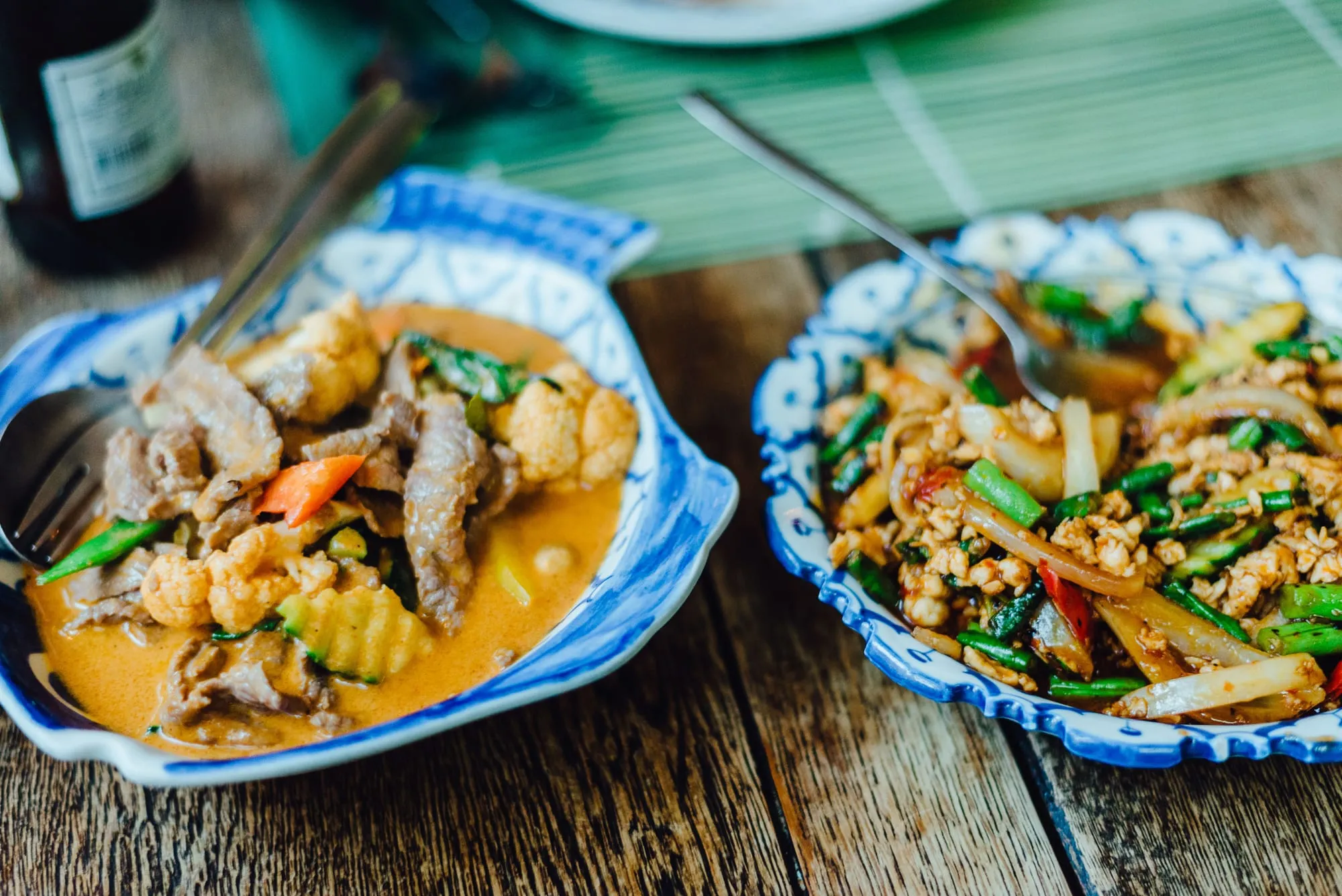 Thai curry and a stir-fry served in blue patterned bowls on a wooden table