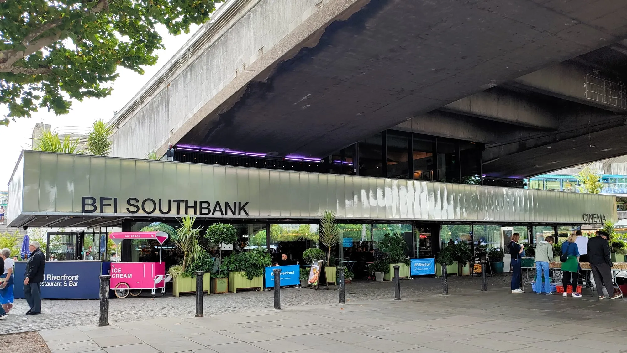 The riverfront entrance to BFI Southbank under Waterloo Bridge, with people outside the bar and the secondhand book market to one side