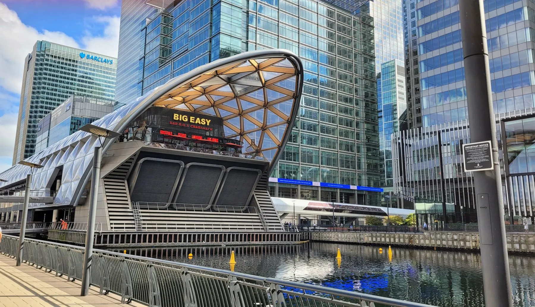 The Big Easy Bar-B-Q and Crabshack sign on the Park Level of Crossrail Place at Canary Wharf, under the timber lattice roof of the building, which rises straight out of the dock water with the towers behind
